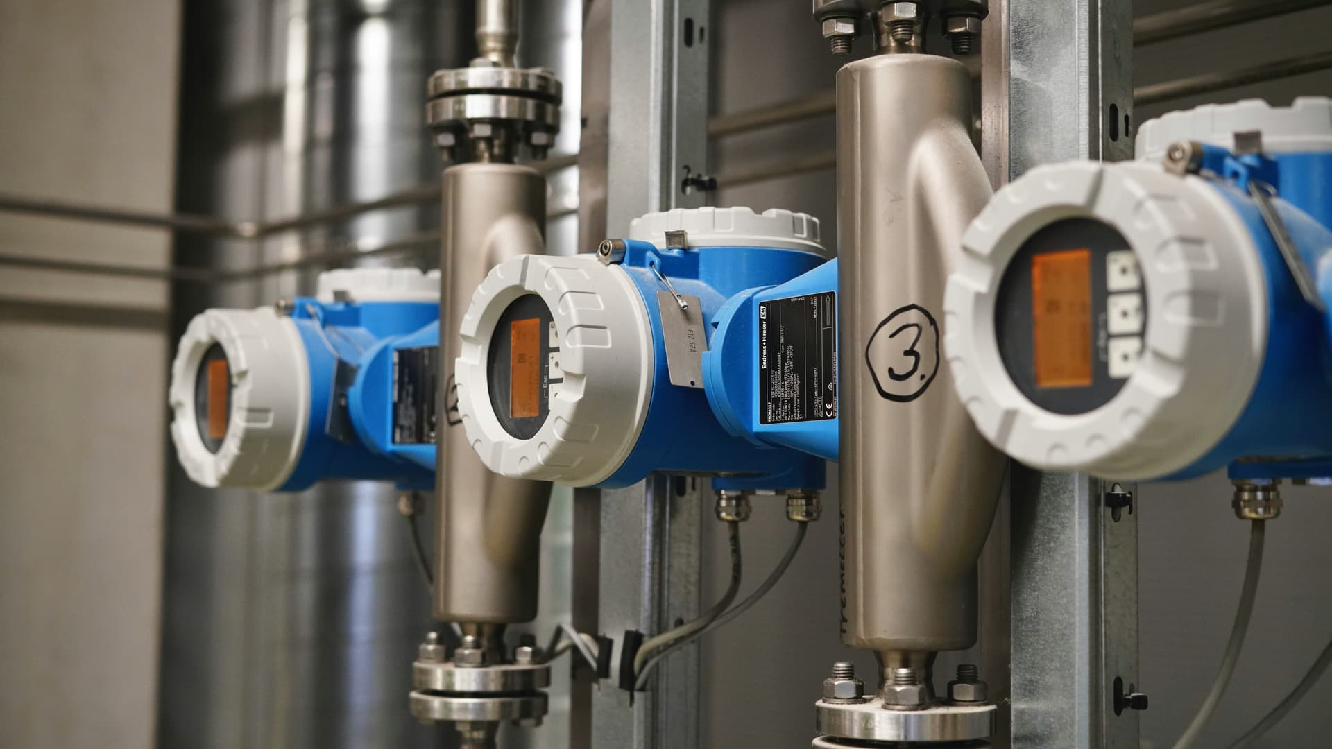 Industrial electromagnetic flow meters and sensors installed on stainless steel pipes — the instrumentation layer that generates the data AI systems need